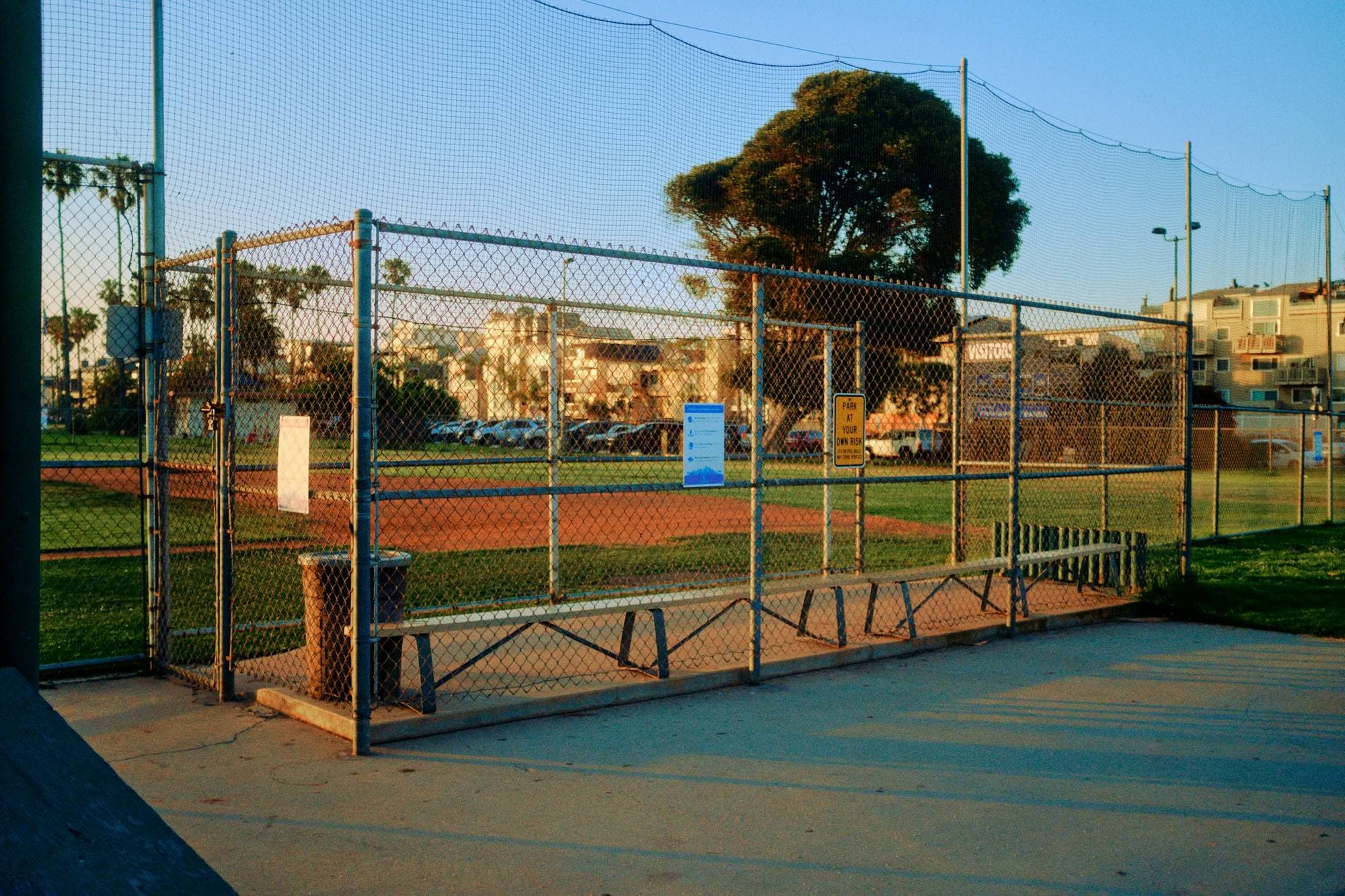 Abri des joueurs grillagé avec banc, en bordure d'un terrain de baseball, sous un ciel bleu