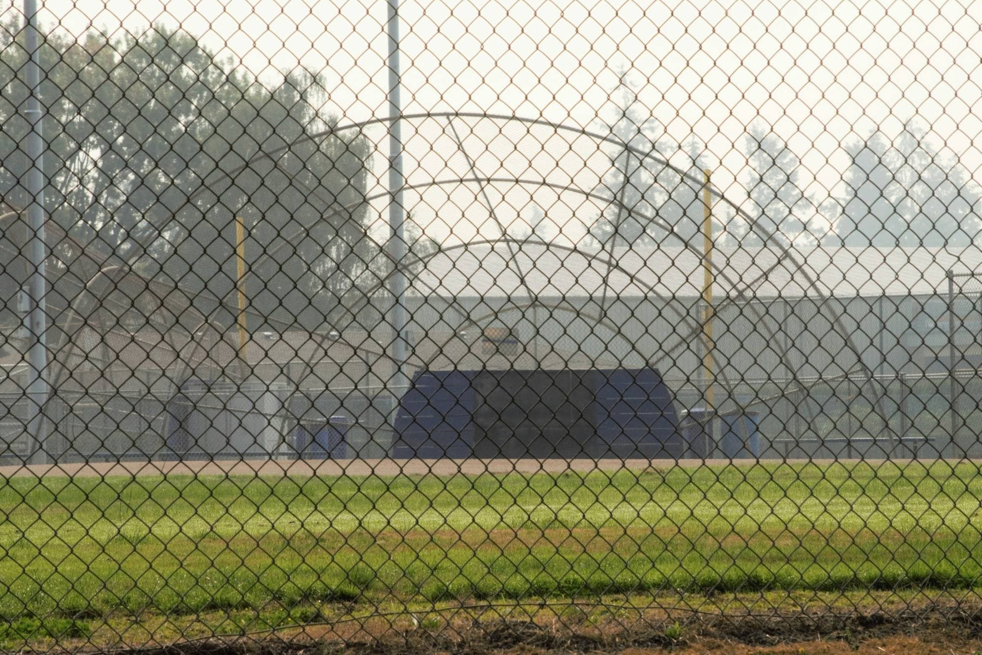 Terrain de baseball derrière un haut grillage d'arrêt, silhouette brumeuse de la ville au loin