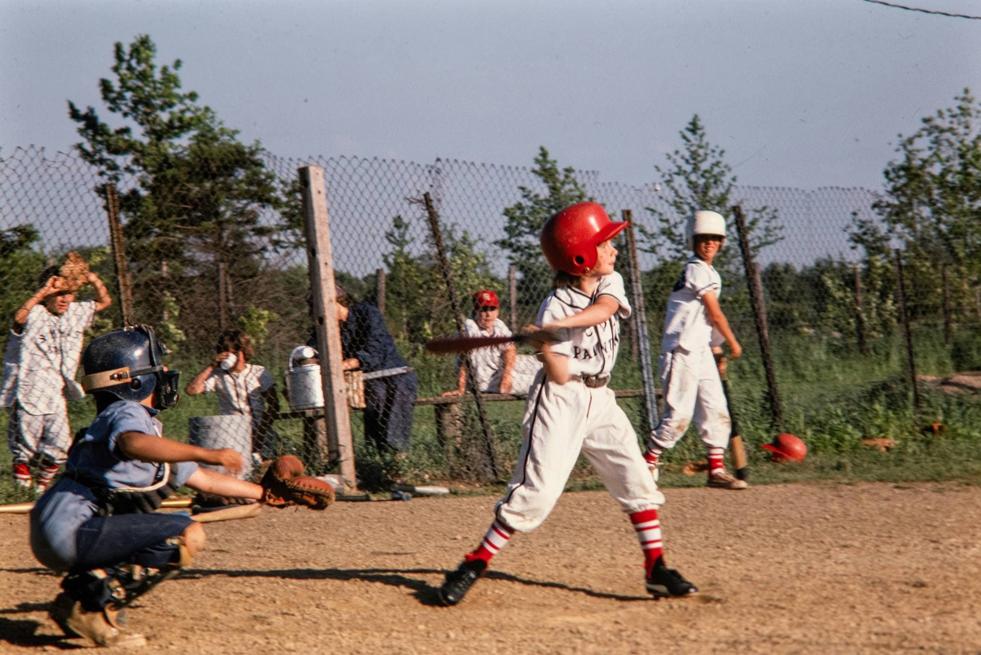 Match de baseball junior : un garçon au casque rouge s'élance au marbre, le receveur accroupi derrière lui