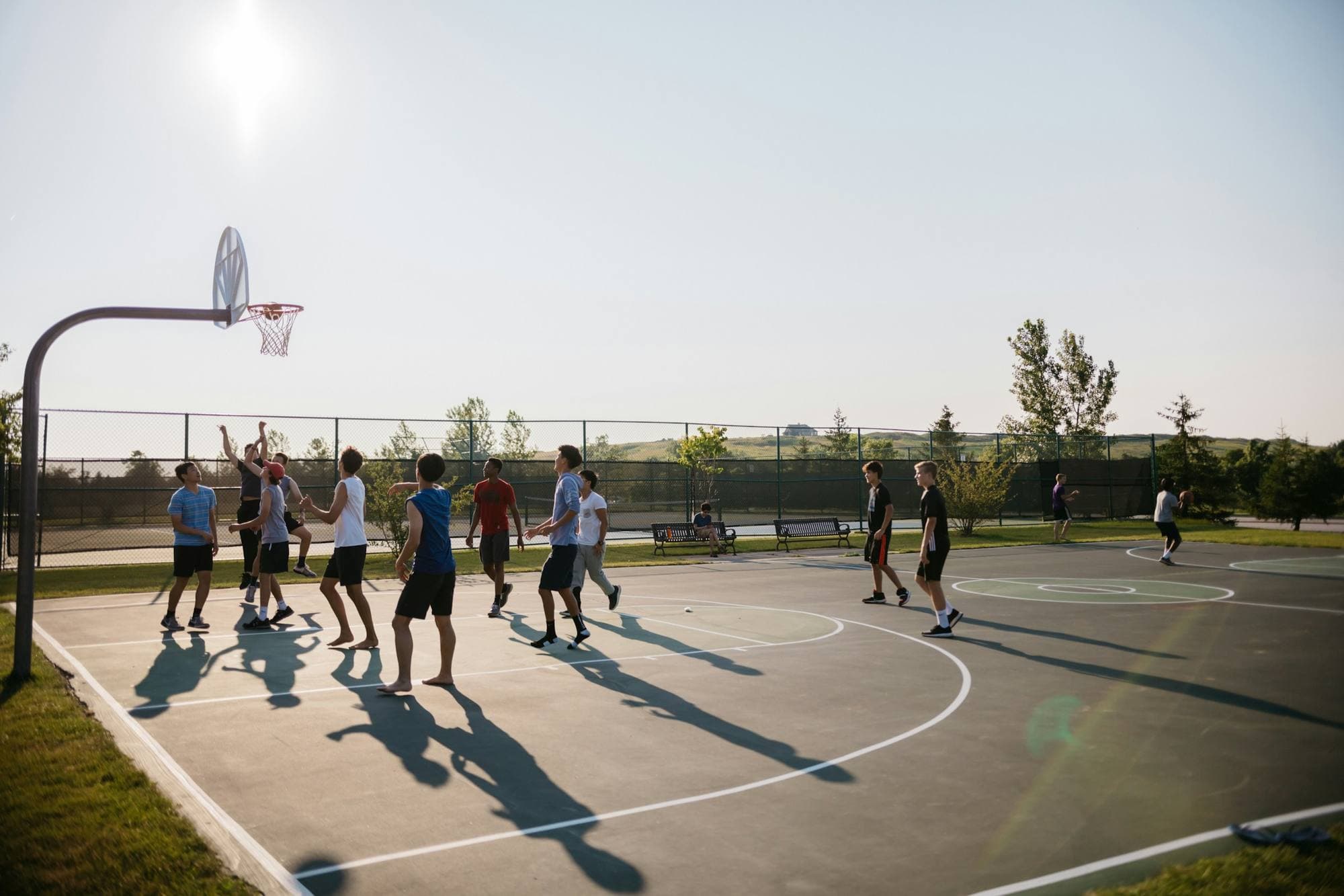 Partie de basketball improvisée sur un terrain extérieur, lumière vive et voilée, longues ombres