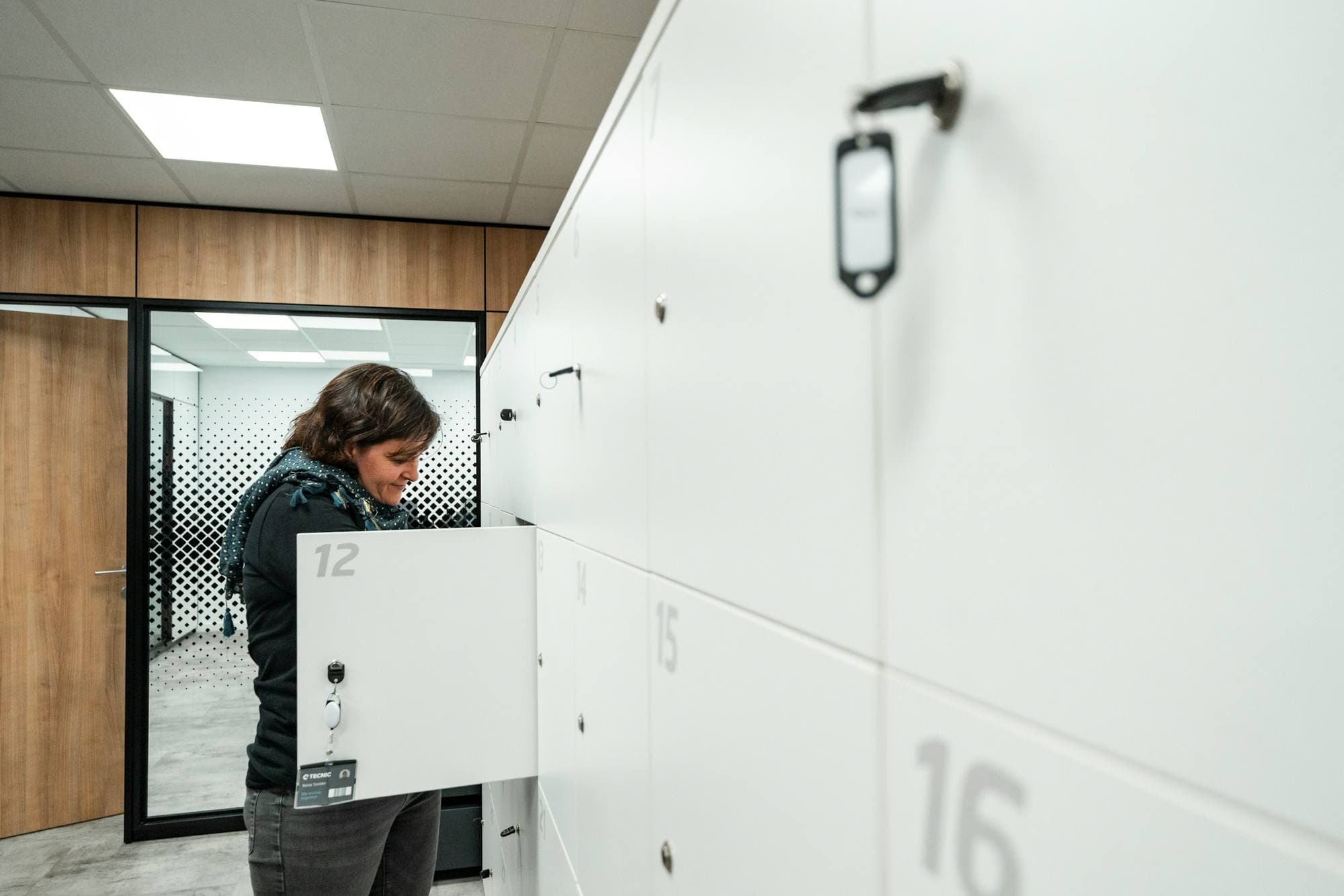 Une femme ouvre un casier blanc à serrure électronique dans un couloir lumineux