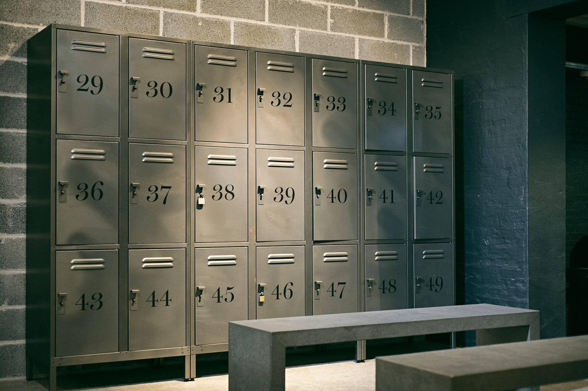 Vestiaire avec casiers métalliques gris numérotés et bancs en béton
