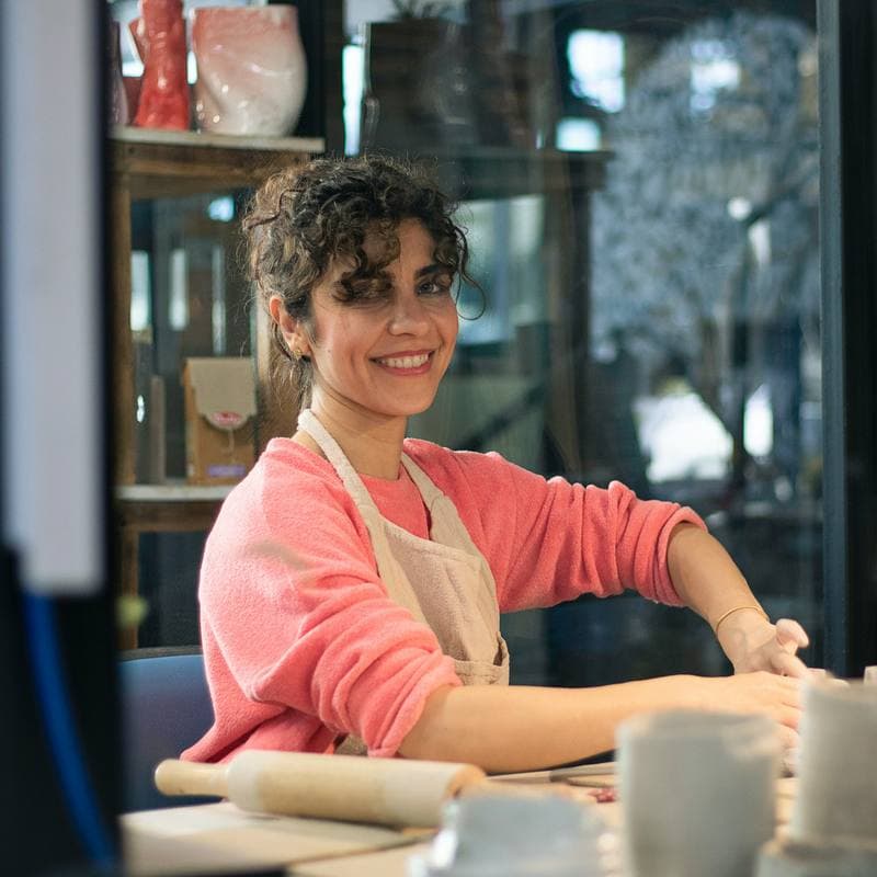 Céramiste souriante en tablier de lin, à sa table de travail dans son atelier