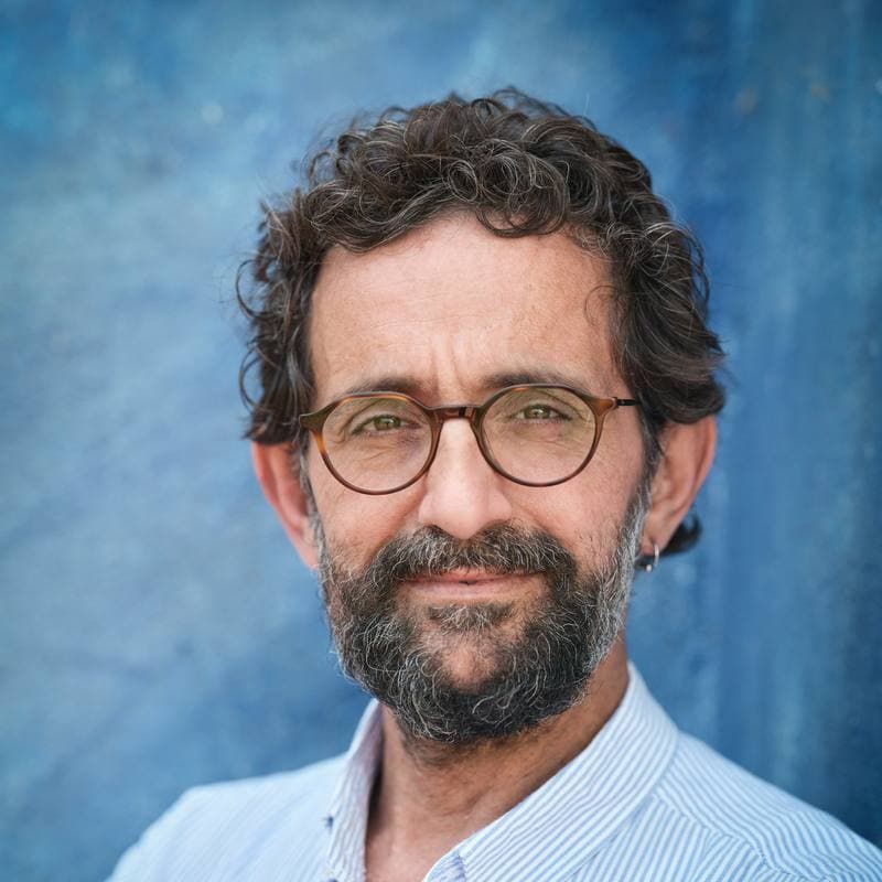 Portrait d'un homme barbu à lunettes, en chemise rayée, devant un mur bleu