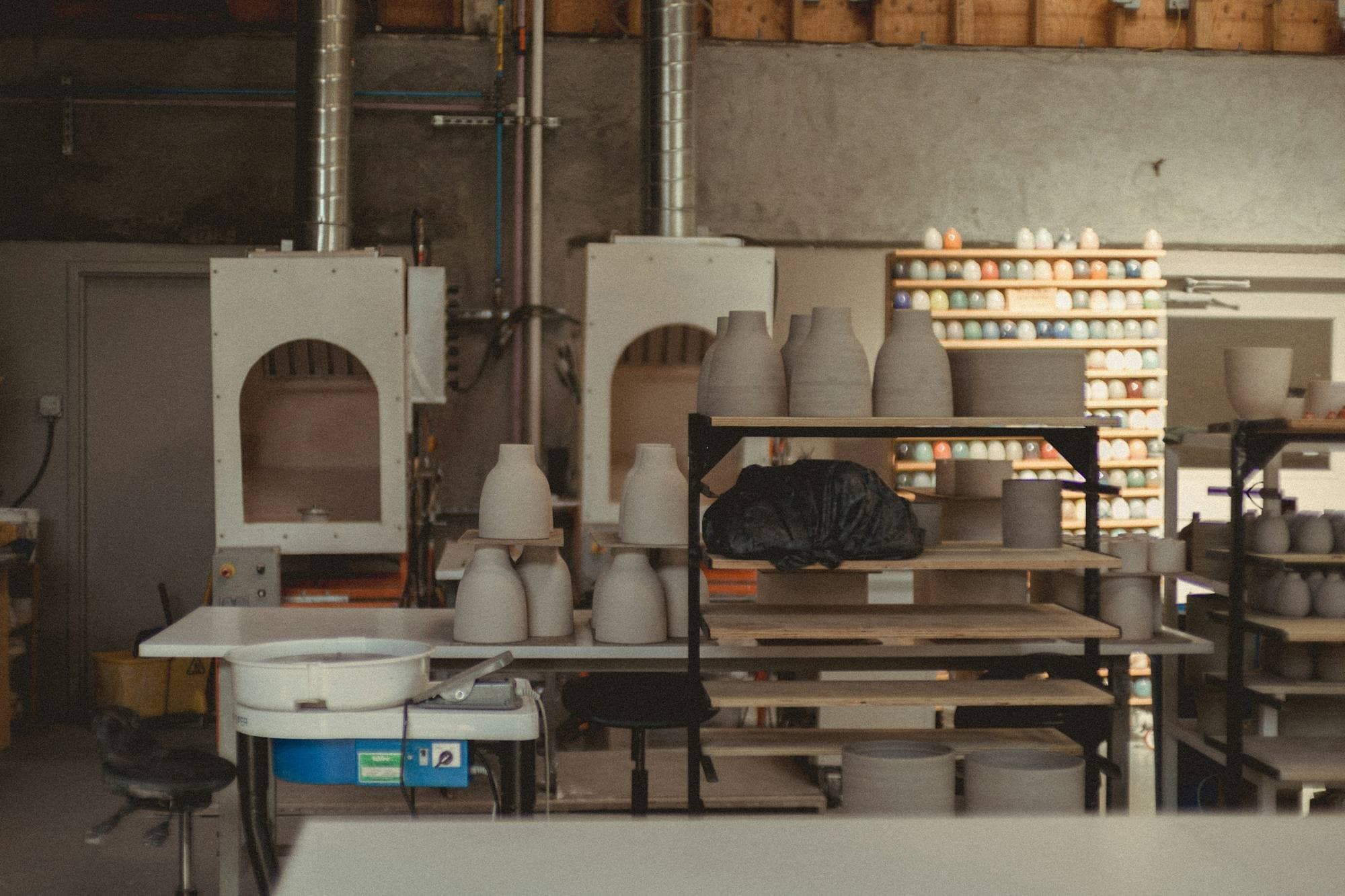 Atelier de céramique avec deux fours, étagères de pièces biscuitées et table de travail