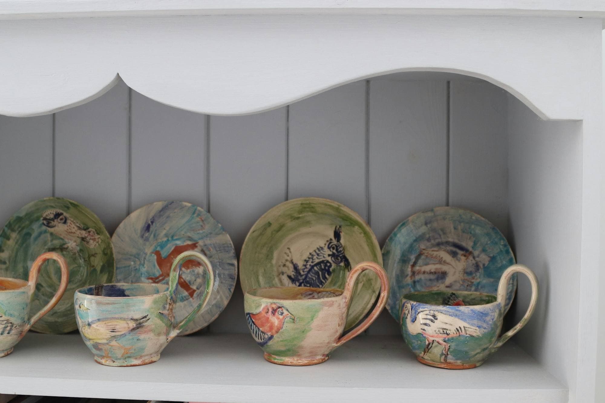Tasses et soucoupes émaillées peintes à la main, alignées sur une étagère blanche