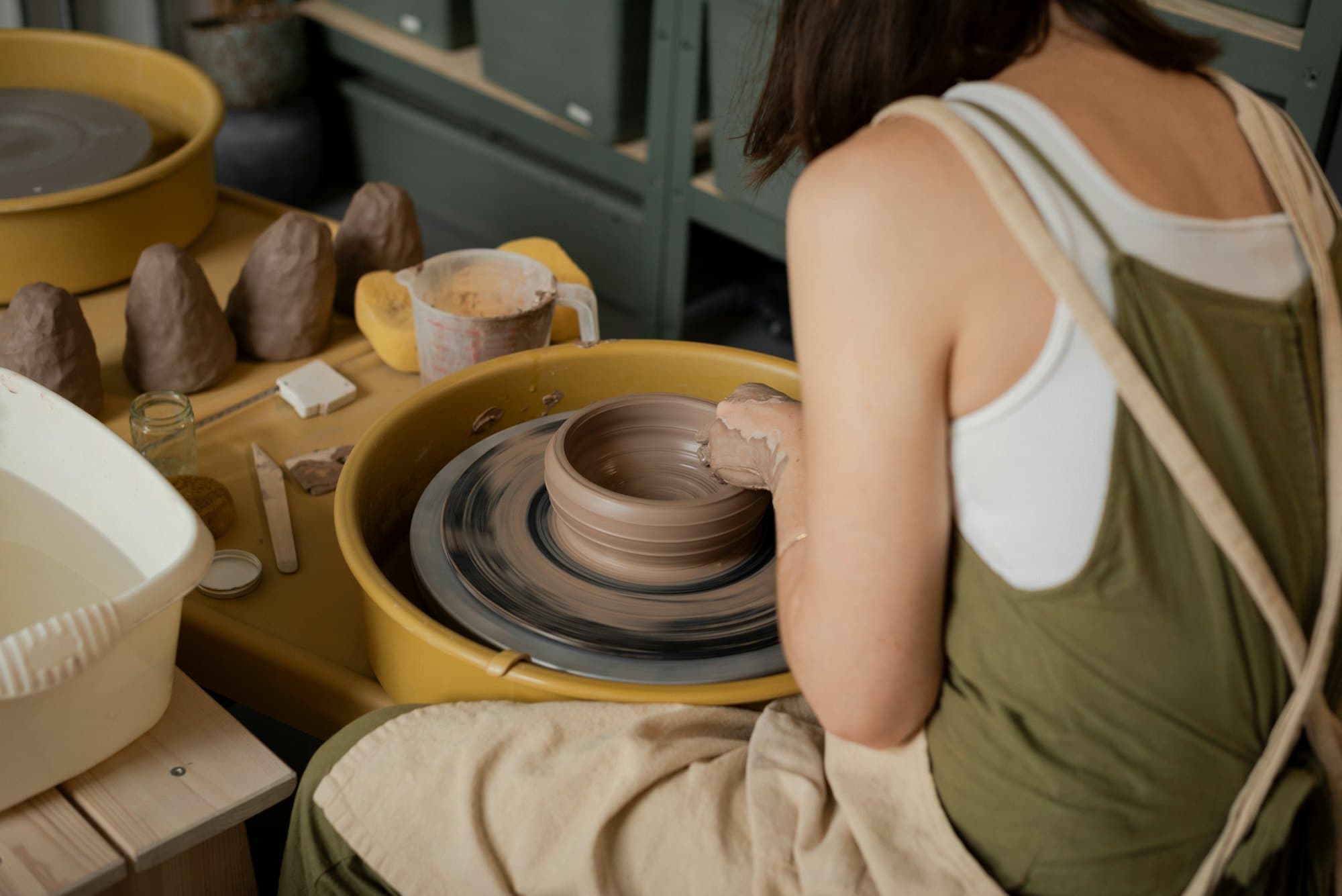Une potière façonne l'argile au tour, entourée d'outils et de pots frais