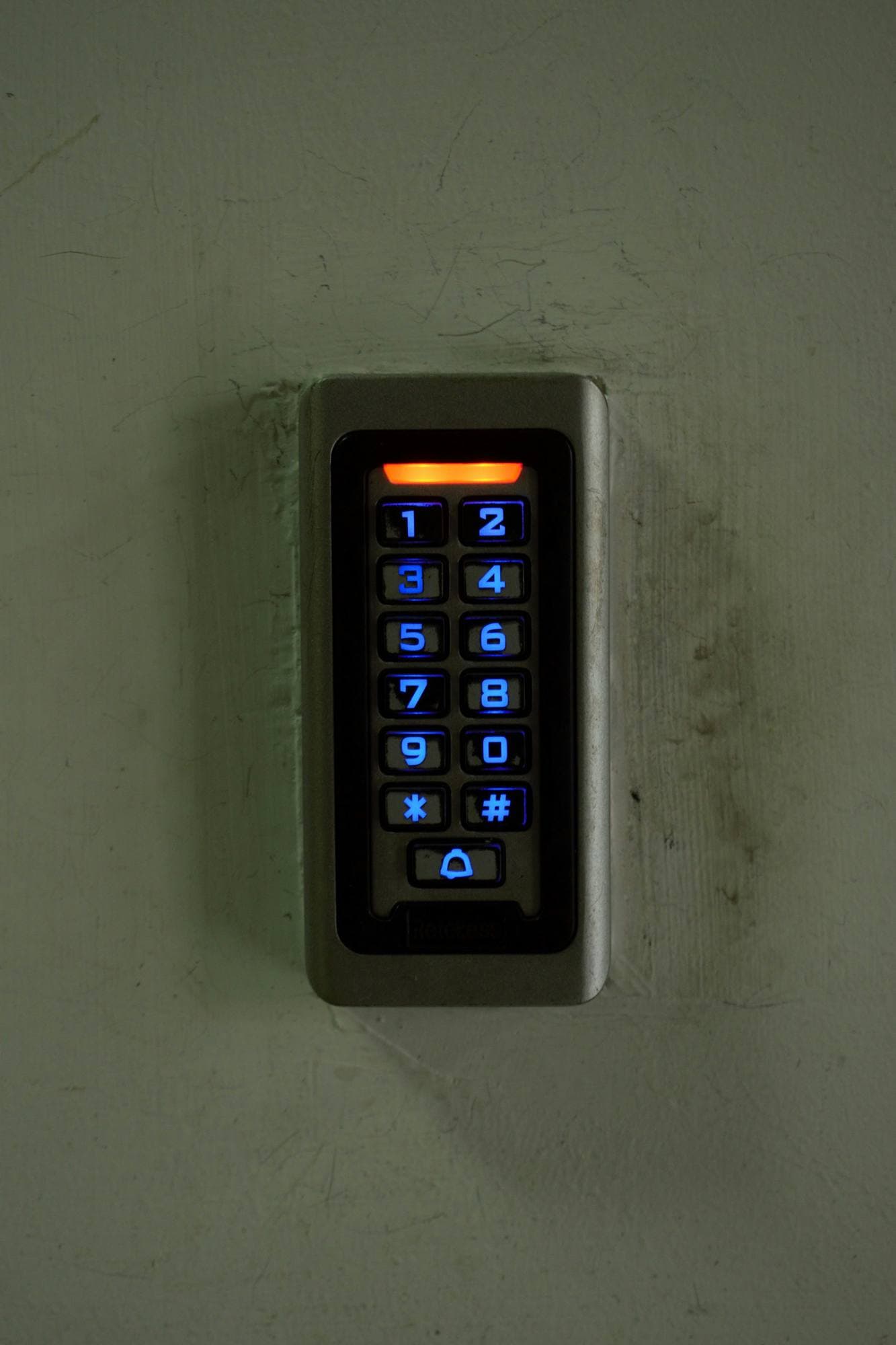 Clavier numérique rétroéclairé fixé sur un mur gris-vert près d'une porte