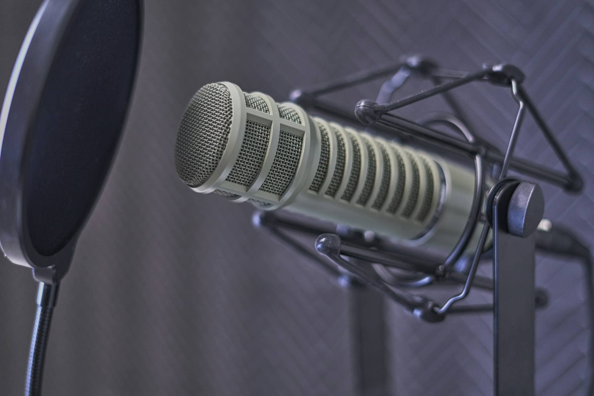 Microphone de studio avec filtre anti-pop sur suspension, devant un mur gris ardoise